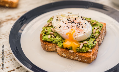Close up food photography of an avocado toast with poached egg and sesame seeds. Breakfast, lunch, brunch, light dinner dish meal, vegetarian food, healthy eating concept.