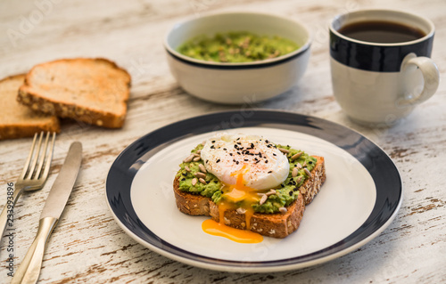 Food photography of an avocado toast with poached egg, sesame seeds, and black coffee. Breakfast, lunch, brunch, light dinner dish meal, vegetarian food, healthy eating concept.