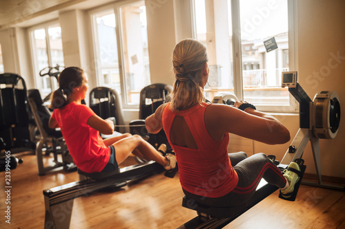 Back view of young fit women working out with rowing machine at gym