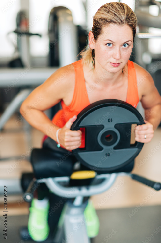 Fototapeta premium Young fit woman working with heavy disk in gym