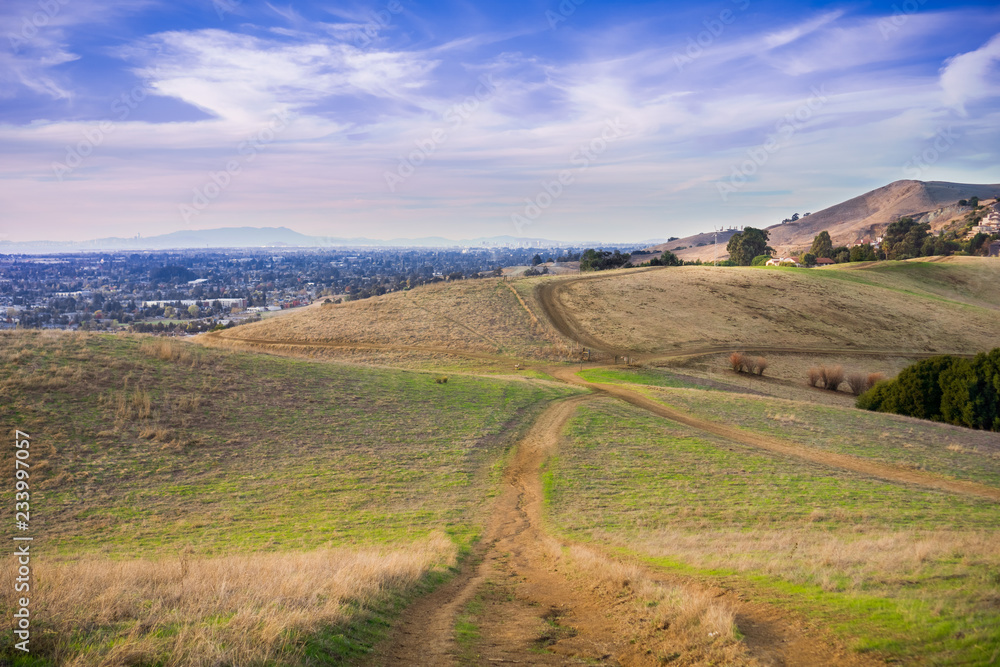 Hiking trail over the hills of Garin Dry Creek Pioneer Regional Park at sunset, Oakland and San Francisco skyline in the background, California