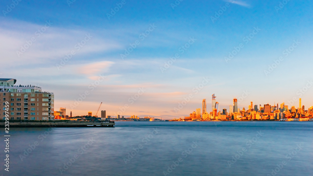 Skyline of uptown Manhattan over Hudson River under blue sky, at sunset, in New York City, USA