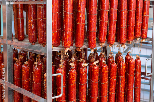 Smoked sausage suspended on a rope on a metal frame in the smokehouse.