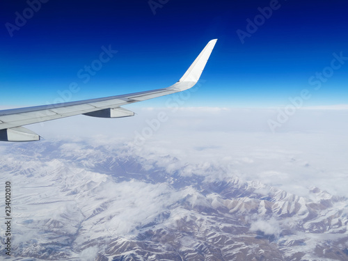 Wing of an airplane flying above the snow mountains in Southwest China. The view from an airplane window. Travel concept.