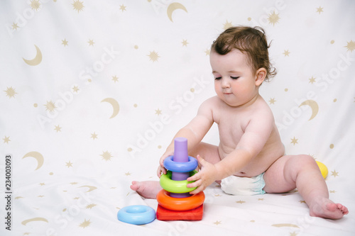 Baby in a diaper sitting and playing a colorful pyramid