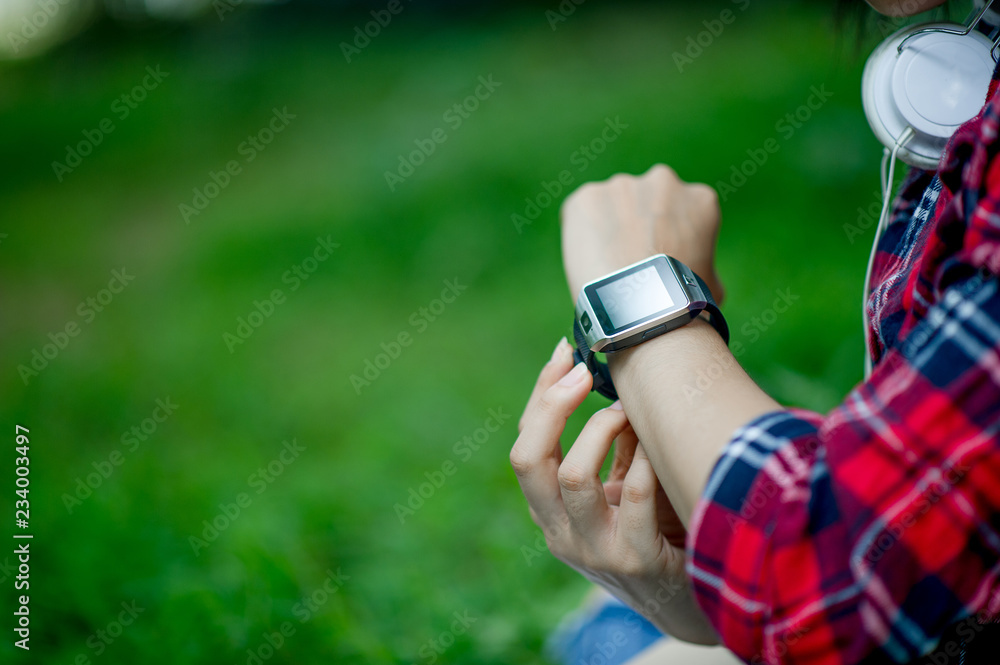 The girl watches the watch in hand, watches the time in a black watch, wears a red shirt and a green background. And there is a copy space. The girl watches the watch in hand, watches the time in a black watch, wears a red shirt and a green background. And there is a copy space.