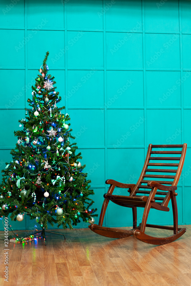 Christmas tree and rocking chair against the background of the turquoise wall.
