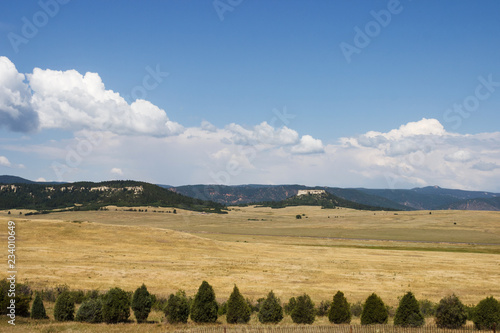 Scenic mountains, clear deep sky with white clouds on a summer sunny day. At the foot of the mountains are located houses of small American cities. Colorado, USA.