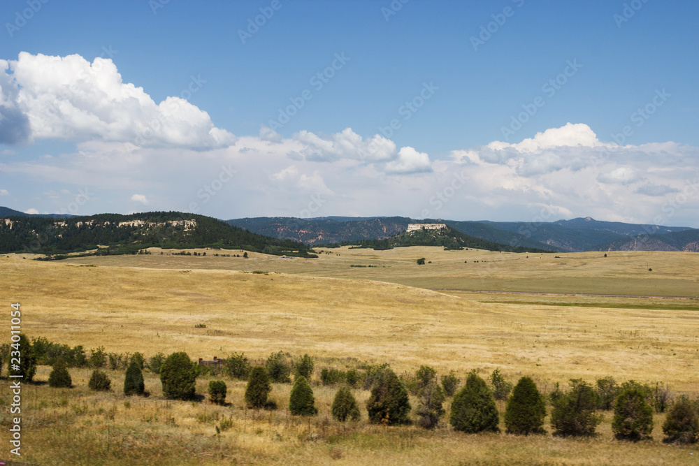 Obraz premium Scenic mountains, clear deep sky with white clouds on a summer sunny day. At the foot of the mountains are located houses of small American cities. Colorado, USA.