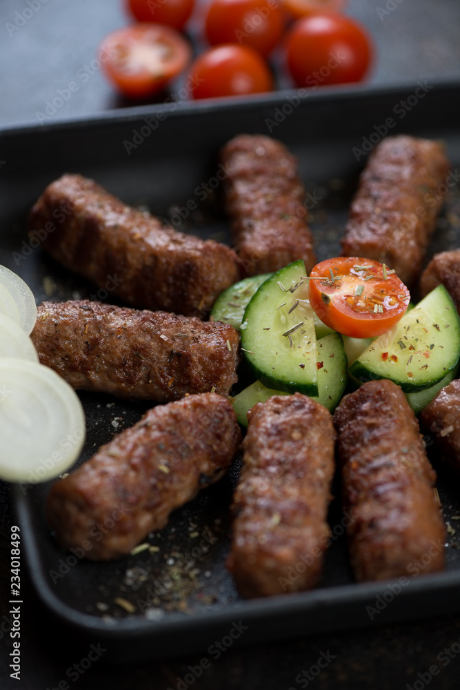 Barbecued cevapcici or skinless beef sausages with cucumber, tomatoes and onion, closeup, selective focus Barbecued cevapcici or skinless beef sausages with cucumber, tomatoes and onion, closeup, selective focus