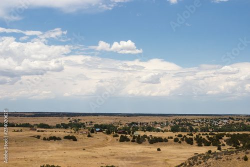 Landscape with houses in the distance on a summer day. Steppe. Hills overgrown with dry grass.