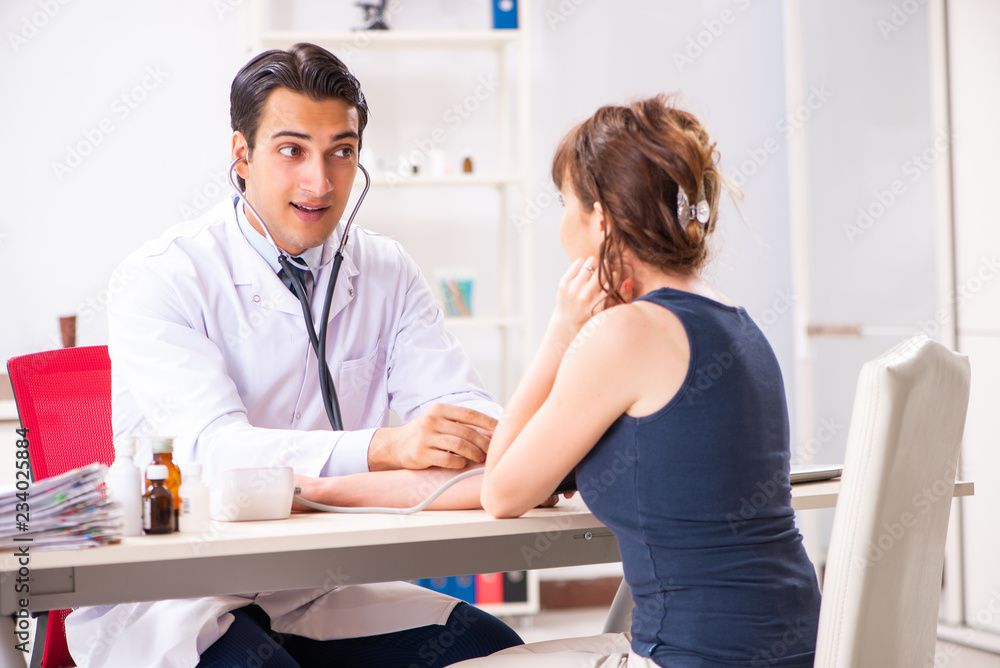 Fototapeta premium Young doctor checking woman's blood pressure