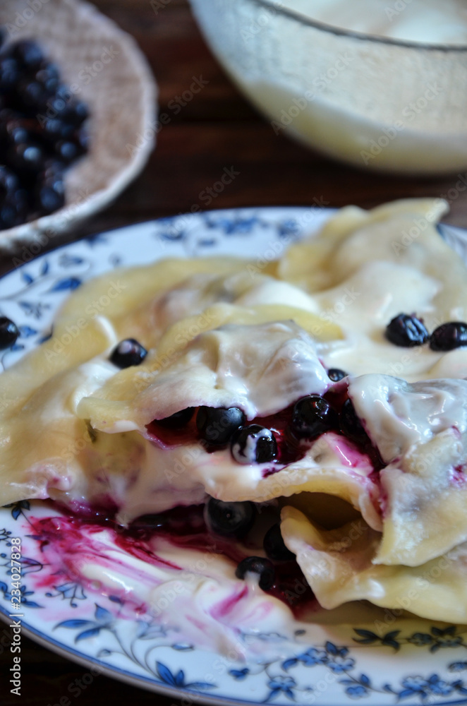 Fotografi Pierogi with blueberries topped with cream on a plate on a wooden background