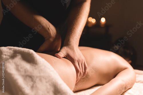 Close-up male hands doing healing massage with oil to a young girl in a dark cosmetology office. Dark key
