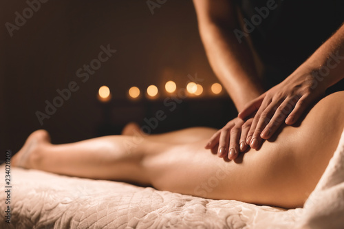 A masseur in a dark room does a hip massage with oil for a woman. Spa procedures massage women