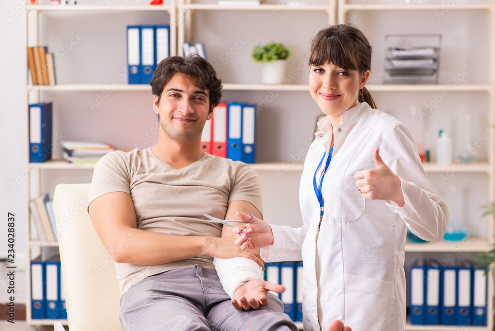 Young man with bandaged arm visiting female doctor traumatologis Young man with bandaged arm visiting female doctor traumatologis