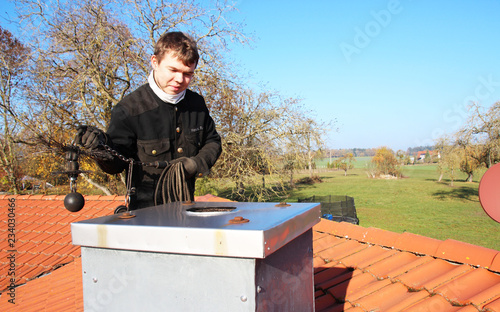 A chimney sweeper sitting on a flue on top of the roof