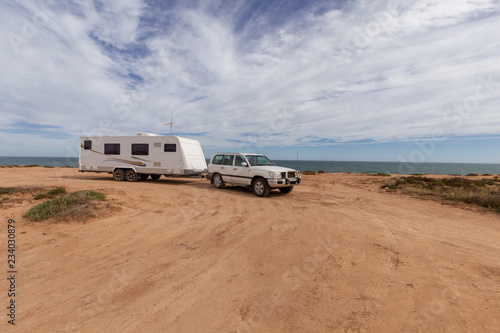 Caravan and Four wheel drive vehicle parked on low orange cliffs next to a beach.