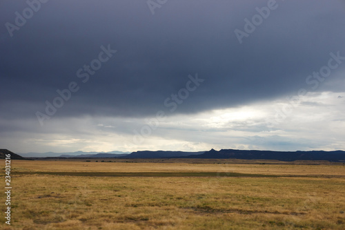 Summer day, dark sky, big dark blue clouds in the sky. In the steppe before the rain. Dark blue mountains on the horizon