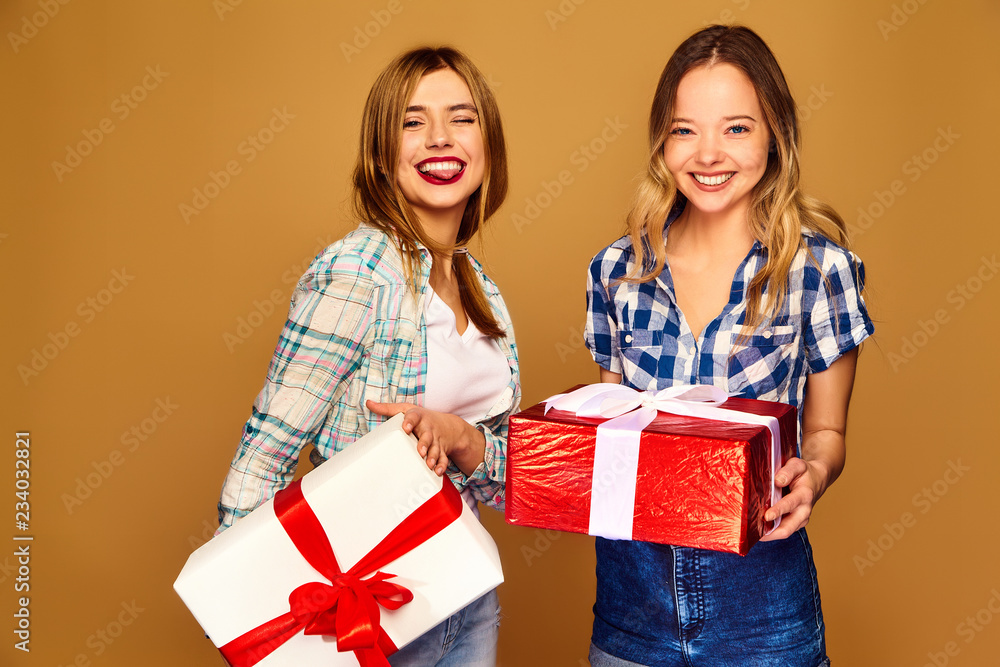 Christmas, x-mas, concept.Two smiling beautiful women in stylish clothes.Girls posing on golden background.Models with big gift boxes.Having fun,ready for celebration.Bright holiday of best friends Christmas, x-mas, concept.Two smiling beautiful women in stylish clothes.Girls posing on golden background.Models with big gift boxes.Having fun,ready for celebration.Bright holiday of best friends