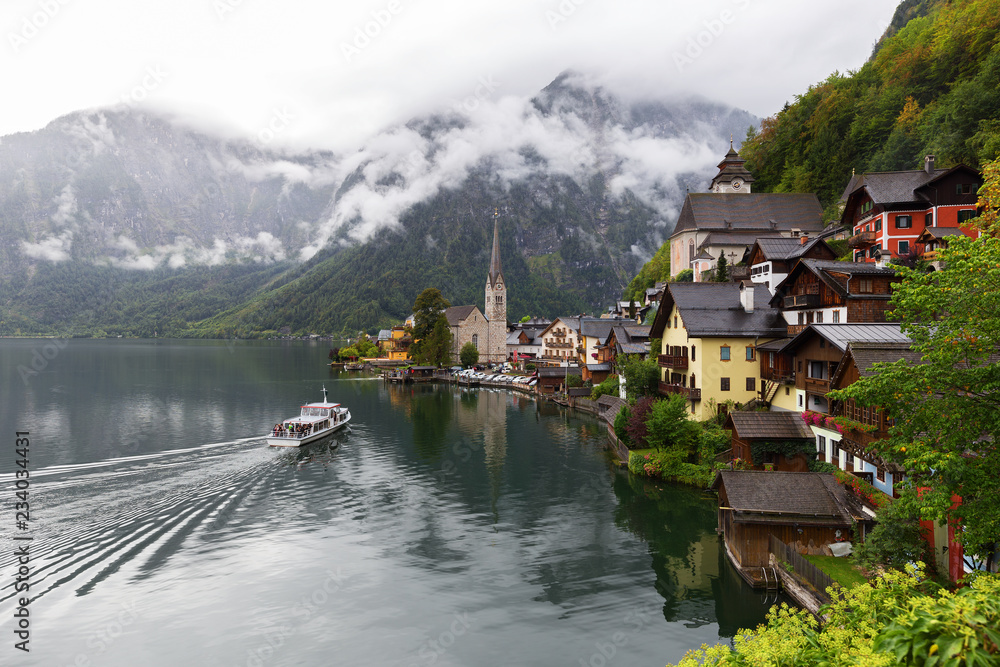 Fototapeta premium Scenic picture-postcard view of famous Hallstatt lakeside town in the Austrian Alps with passenger ship in beautiful morning light at sunrise on a sunny day in summer, Salzkammergut region, Austria