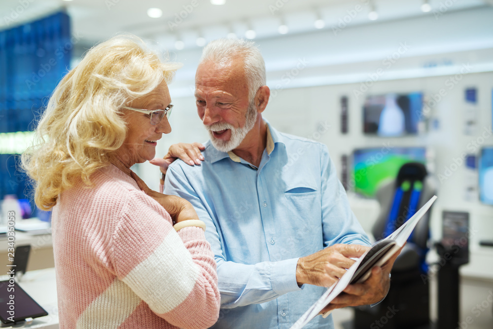 Happy senior couple looking at catalog while standing in tech store.