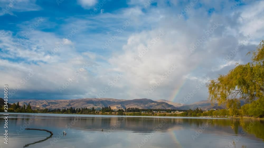 Timelapse video of rainbow in the sky with heavy clouds above peaceful river. Shot in Central Otago, New Zealand. Timelapse video of rainbow in the sky with heavy clouds above peaceful river. Shot in Central Otago, New Zealand.