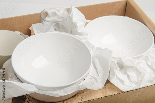 Clean white dishes in paper packed in a cardboard box. Concept relocation.