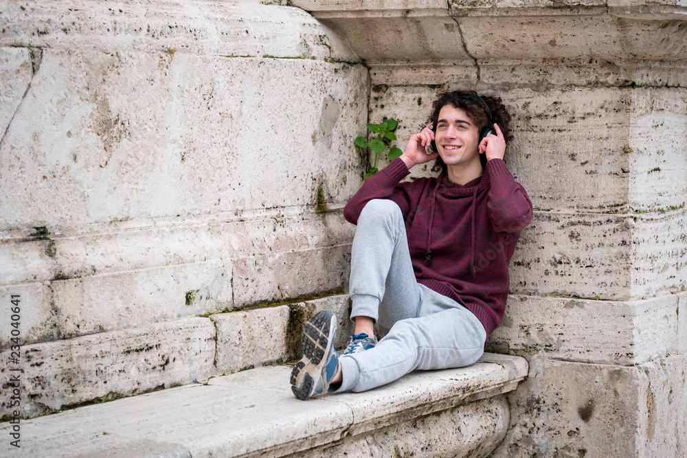 Handsome young man listening to music with headphones on his head. Young man relaxing in front of stone wall
