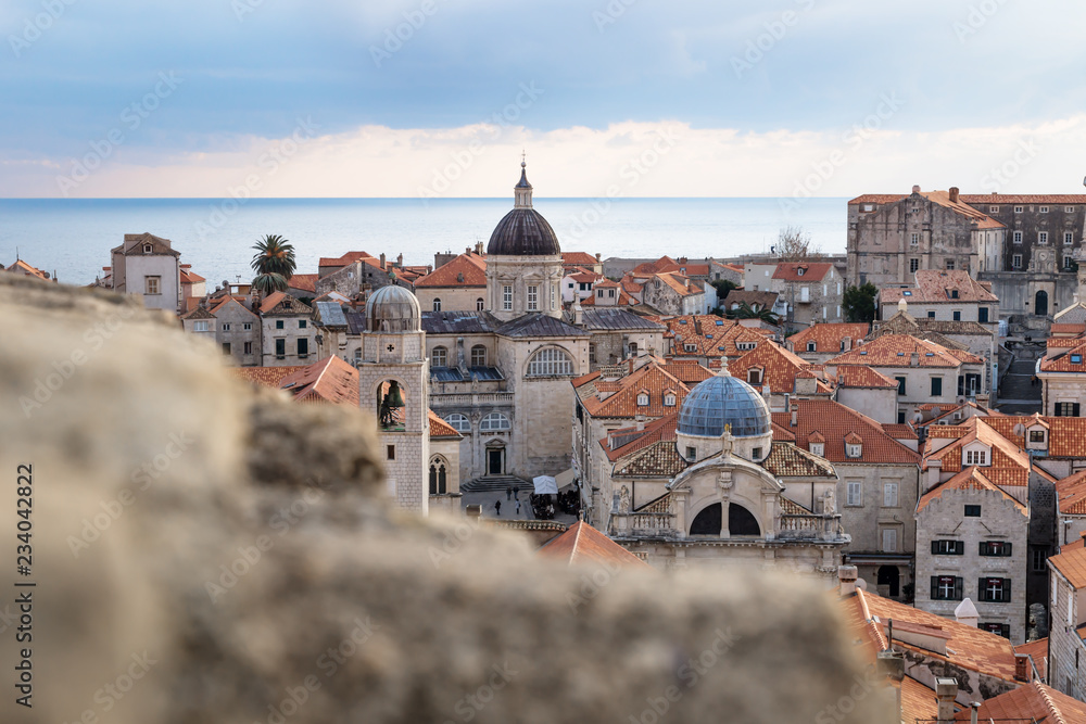 View over the roofs of old town Dubrovnik with church towers and ocean behind a stone wall in winter, Croatia