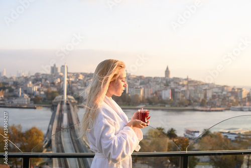 A girl in a bathrobe with a cup of Turkish tea at sunrise on the terrace of a house in Istanbul