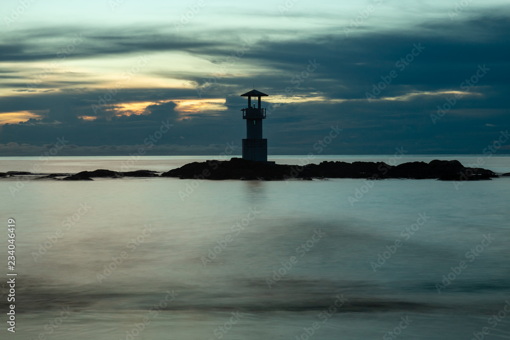 Long exposure image of a small lighthouse against a tropical ocean sunset and smooth water