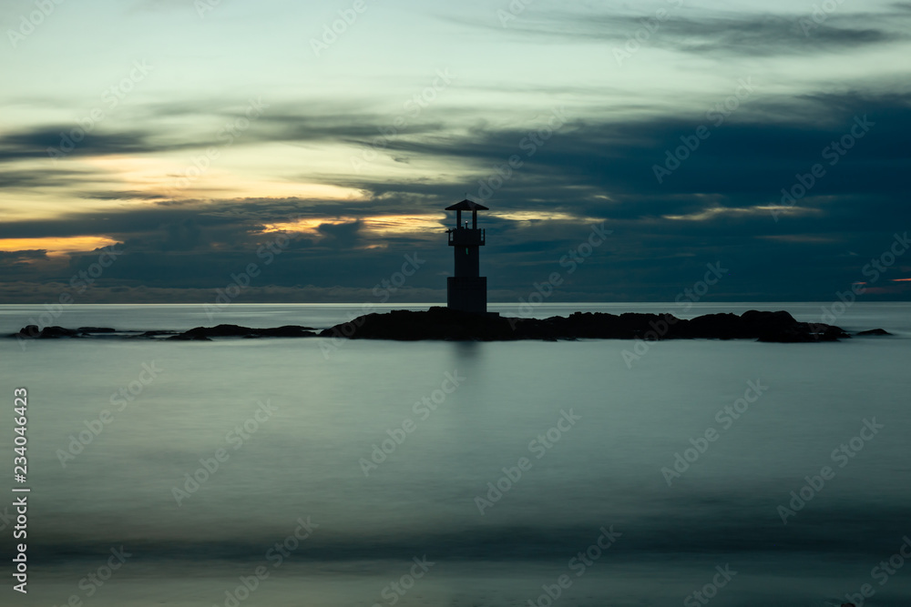 Long exposure image of a small lighthouse against a tropical ocean sunset and smooth water