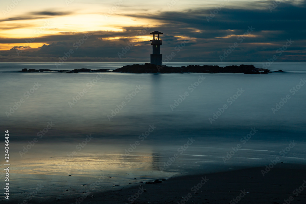 Long exposure image of a small lighthouse against a tropical ocean sunset and smooth water