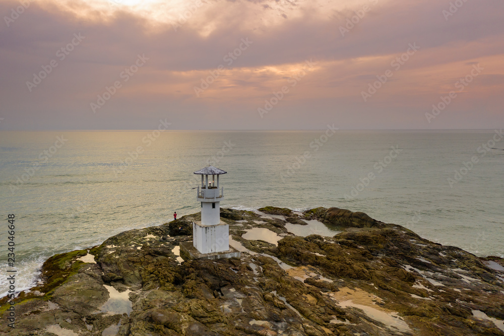 Aerial drone view of a small lighthouse on a rocky island just off a sandy beach and rough sea