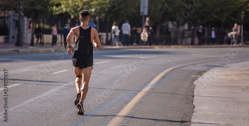 Running in the city roads. Young man runner, back view, blur background