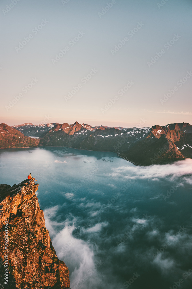 Norway vacations travel man sitting on the edge cliff mountains above sea alone adventure lifestyle weekend trip getaway