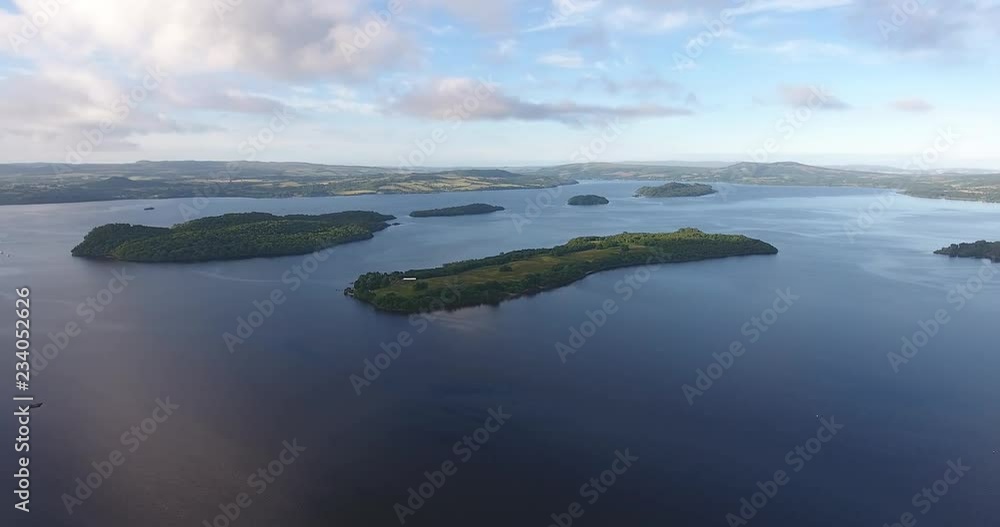 Scottish Loch Featuring a Distant Landscape with Green Hills - Loch Lomond inside The Trossachs National Park Scottish Loch Featuring a Distant Landscape with Green Hills - Loch Lomond inside The Trossachs National Park