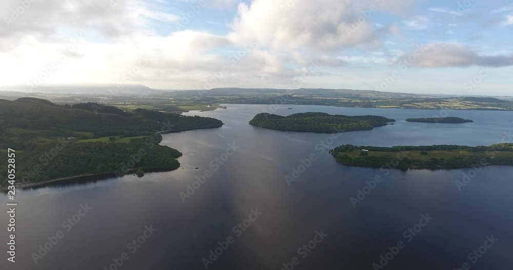Scottish Loch Featuring a Distant Landscape with Green Hills - Loch Lomond inside The Trossachs National Park Scottish Loch Featuring a Distant Landscape with Green Hills - Loch Lomond inside The Trossachs National Park