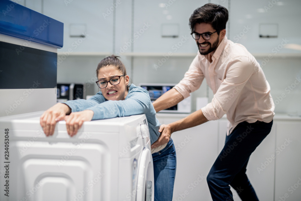 Obraz premium Man taking away wife from washing machine. Whiteware department interior.