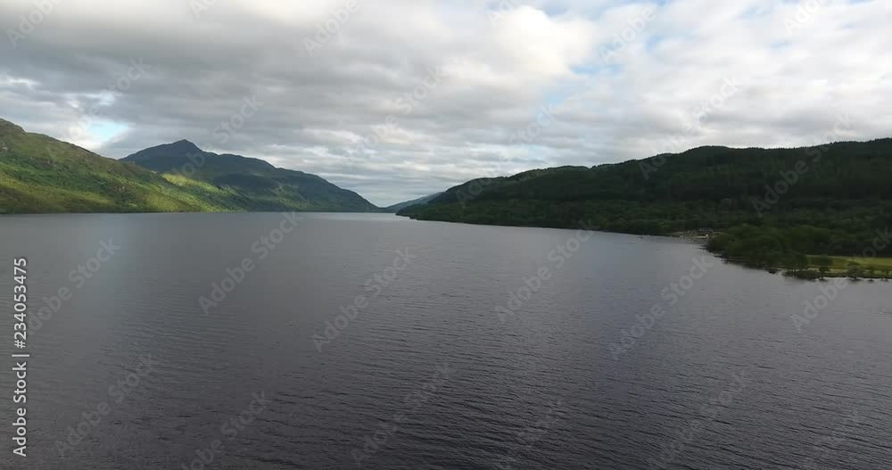 Scottish Loch Featuring a Distant Landscape with Green Hills - Loch Lomond inside The Trossachs National Park Scottish Loch Featuring a Distant Landscape with Green Hills - Loch Lomond inside The Trossachs National Park