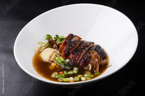 Asian duck noodle soup served with leek and herbs in a white bowl