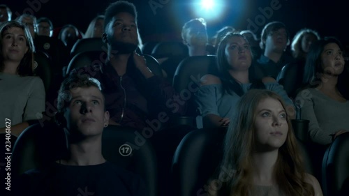 Wide shot of young movie theatre audience sitting, watching a movie. Slow dolly left to right.