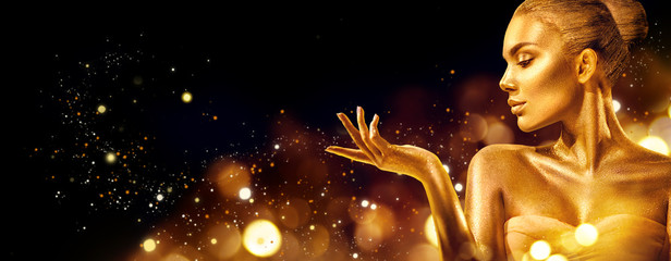 Gold Christmas woman. Beauty fashion model girl with golden makeup, hair and jewellery pointing hand on black background