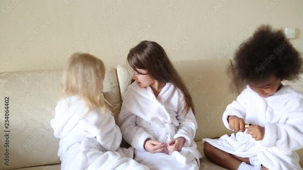 Little girls play with makeup while sitting on the couch. Girls of different nationalities paint their faces with makeup powder cheeks.