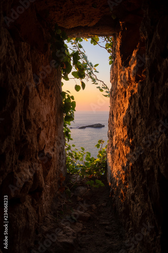 Idyllic Sunset view of a small rocky island from fortress window lit by golden sun, with ivy growing in, Ulcinj Montenegro