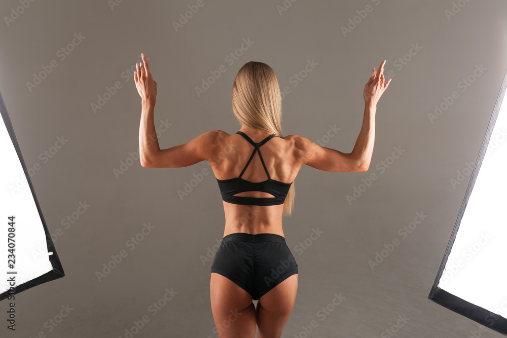 Strong Athletic woman Fitness Model posing back muscles, triceps,  latissimus over black background in the studio. Athletic young woman  showing muscles of the back and hands. Stock Photo