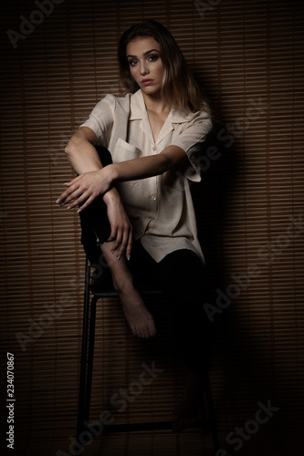 Beautiful young woman sit on chair in a dark moody room with wooden wall