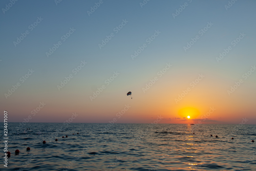 Silhouette of powered paraglider soaring flight over the sea against marvellous orange sunset sky. Paragliding - recreational and competitive adventure sport. Silhouette of powered paraglider soaring flight over the sea against marvellous orange sunset sky. Paragliding - recreational and competitive adventure sport.