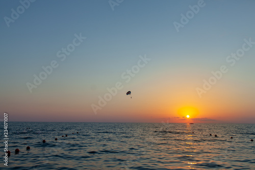 Silhouette of powered paraglider soaring flight over the sea against marvellous orange sunset sky. Paragliding - recreational and competitive adventure sport.